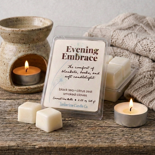 Evening Embrace coconut wax melts in clear packaging resting on a rustic wood surface, featured alongside a ceramic wax warmer, lit tea lights, and a cozy knit blanket.